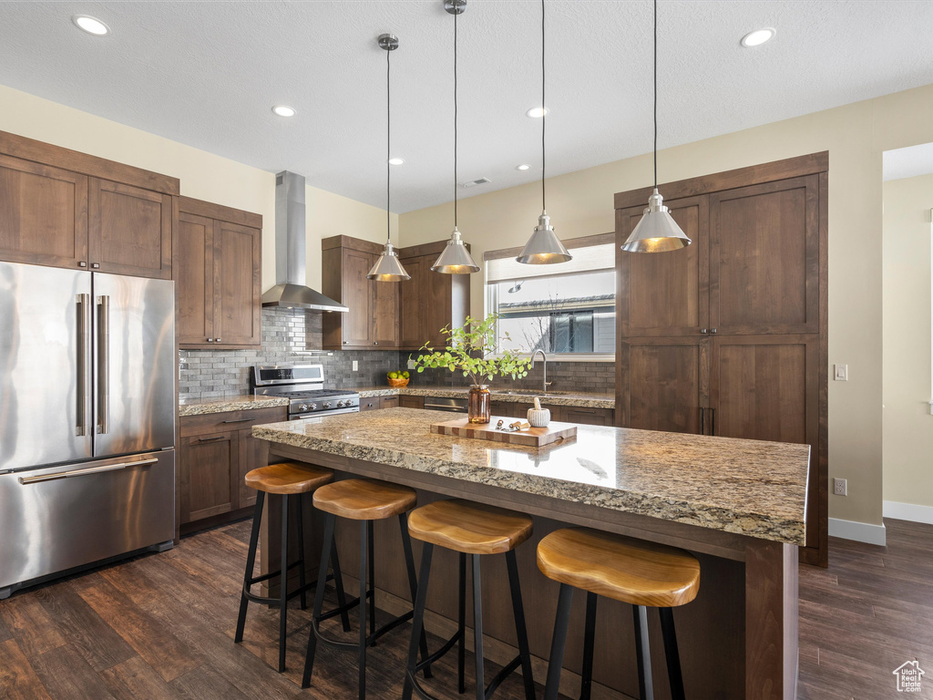 Kitchen with high quality appliances, wall chimney range hood, backsplash, a kitchen breakfast bar, and recessed lighting