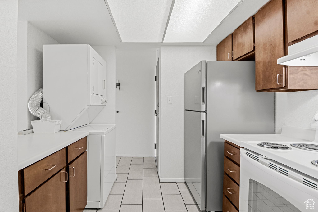 Kitchen featuring electric range, stacked washing machine and dryer, light countertops, light tile patterned flooring, and range hood