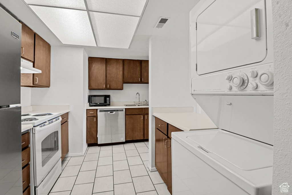 Kitchen with appliances with stainless steel finishes, estacked washer and dryer, a sink, under cabinet range hood, and light countertops