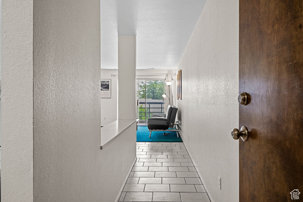 Hallway featuring a textured wall, baseboards, and tile patterned floors