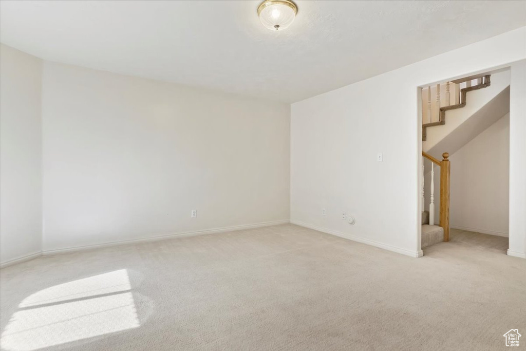 Empty room featuring stairs, light carpet, and baseboards