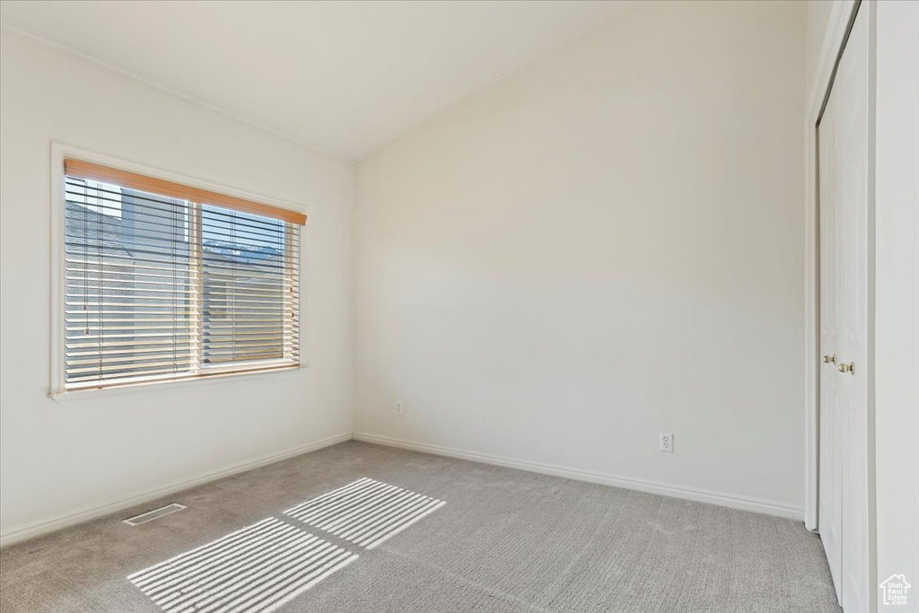 Unfurnished room featuring light carpet, vaulted ceiling, and baseboards
