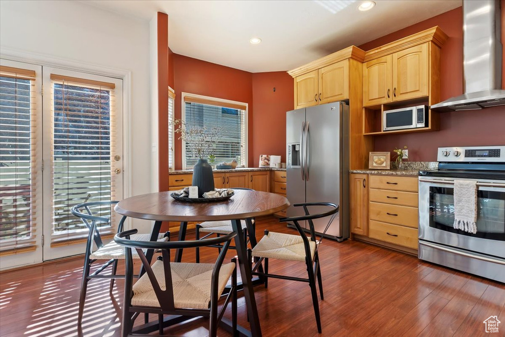 Kitchen with stainless steel appliances, wall chimney range hood, light brown cabinets, dark wood-type flooring, and recessed lighting