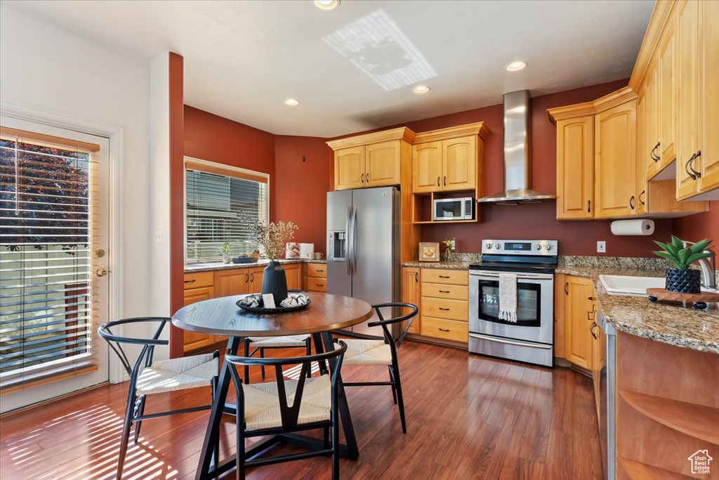 Kitchen featuring appliances with stainless steel finishes, wall chimney exhaust hood, dark wood-style floors, light brown cabinetry, and recessed lighting