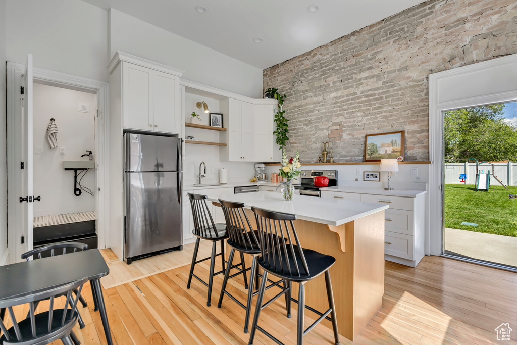 Kitchen with appliances with stainless steel finishes, open shelves, brick wall, light wood-type flooring, and light countertops