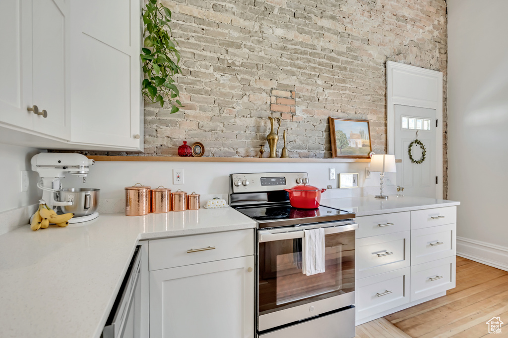 Kitchen with electric stove, brick wall, white cabinets, light countertops, and light wood-type flooring