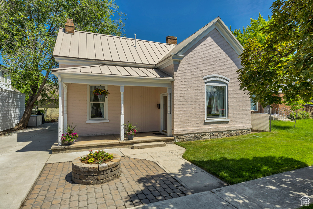 View of front facade with a chimney, a standing seam roof, brick siding, and covered porch