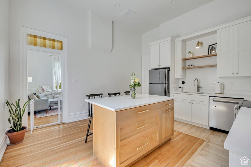 Kitchen with stainless steel appliances, a sink, open shelves, light wood finished floors, and a kitchen breakfast bar