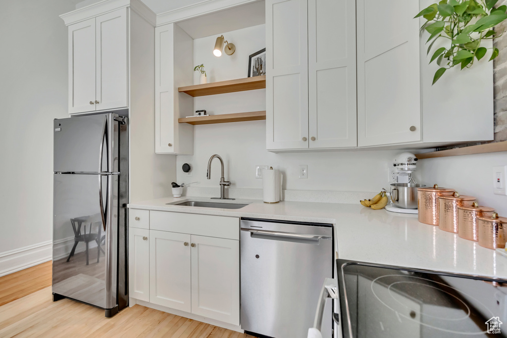 Kitchen featuring stainless steel appliances, a sink, light countertops, open shelves, and white cabinets