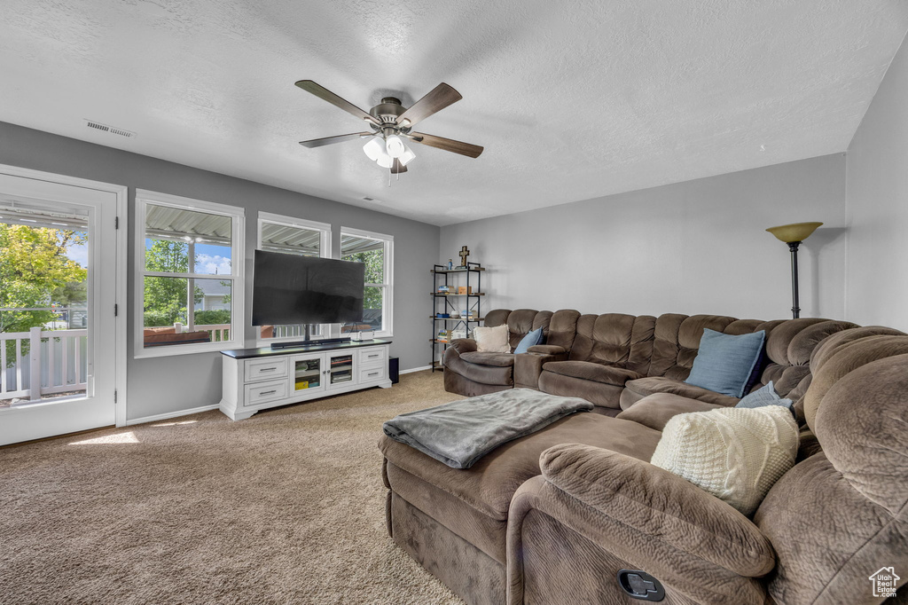 Living area with light colored carpet, a ceiling fan, baseboards, and a textured ceiling