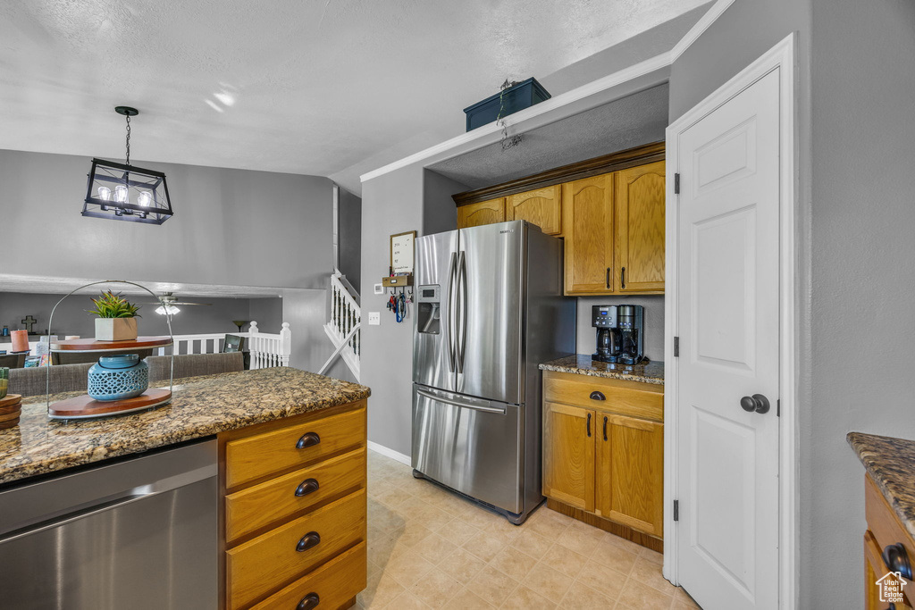 Kitchen featuring stainless steel appliances, dark stone counters, brown cabinets, a ceiling fan, and pendant lighting