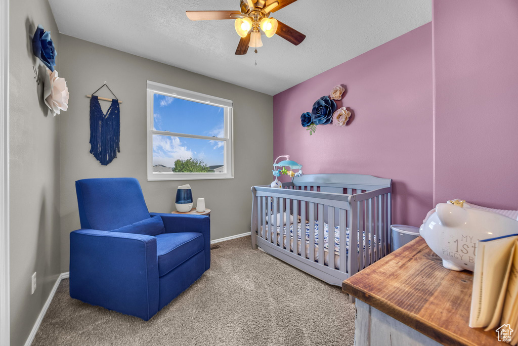 Bedroom with carpet floors, a nursery area, baseboards, ceiling fan, and a textured ceiling