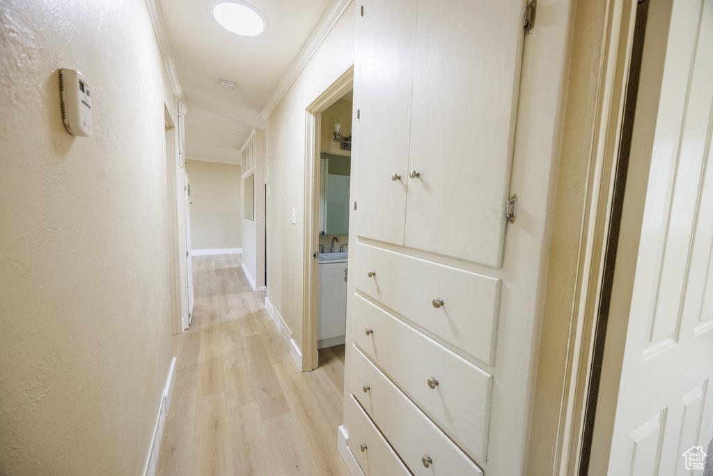 Hallway with light wood finished floors, ornamental molding, baseboards, and a sink