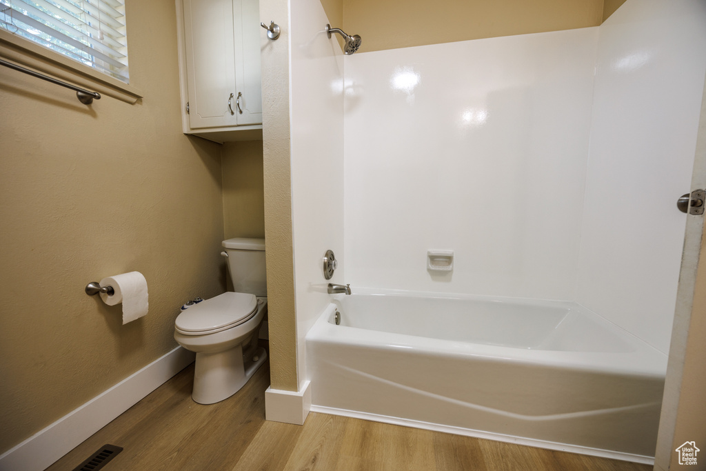 Bathroom with toilet, wood finished floors, bathing tub / shower combination, and baseboards