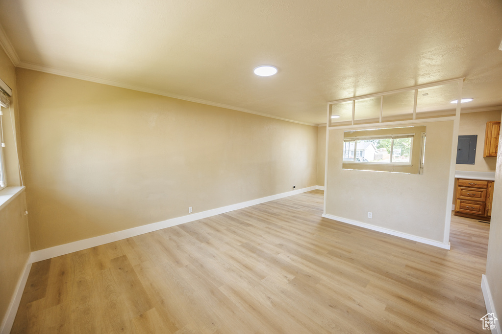 Spare room featuring crown molding, baseboards, electric panel, light wood-style floors, and recessed lighting
