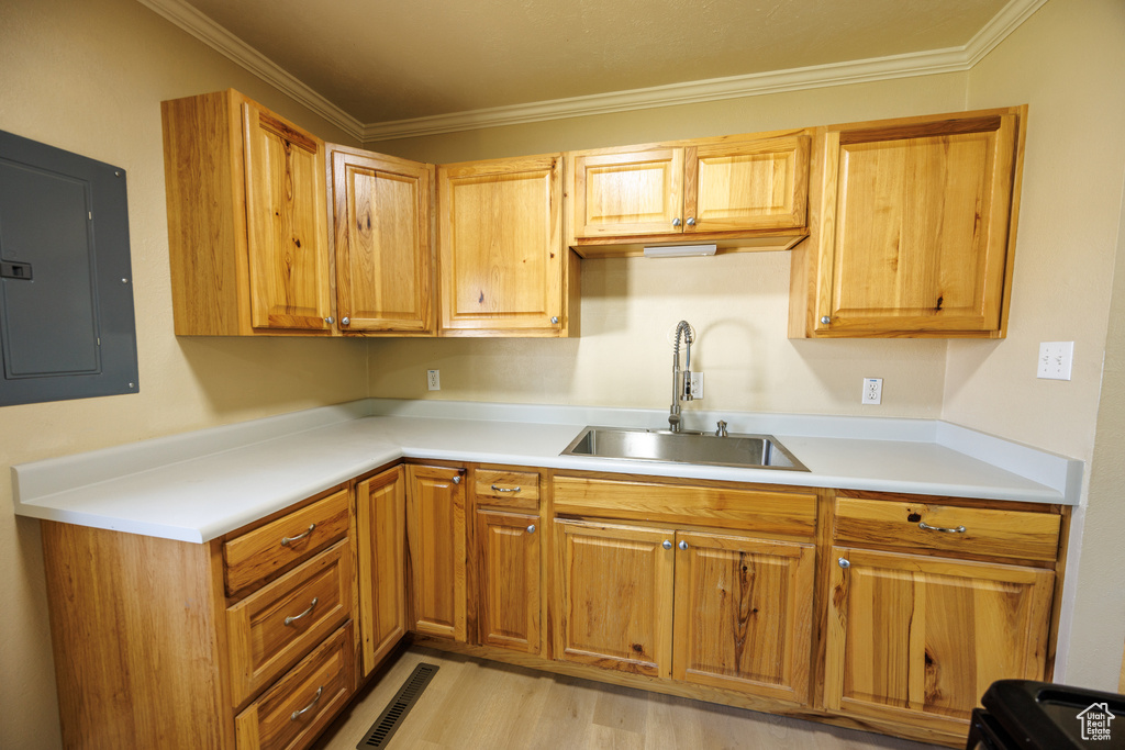 Kitchen with electric panel, a sink, light countertops, light wood-style floors, and ornamental molding