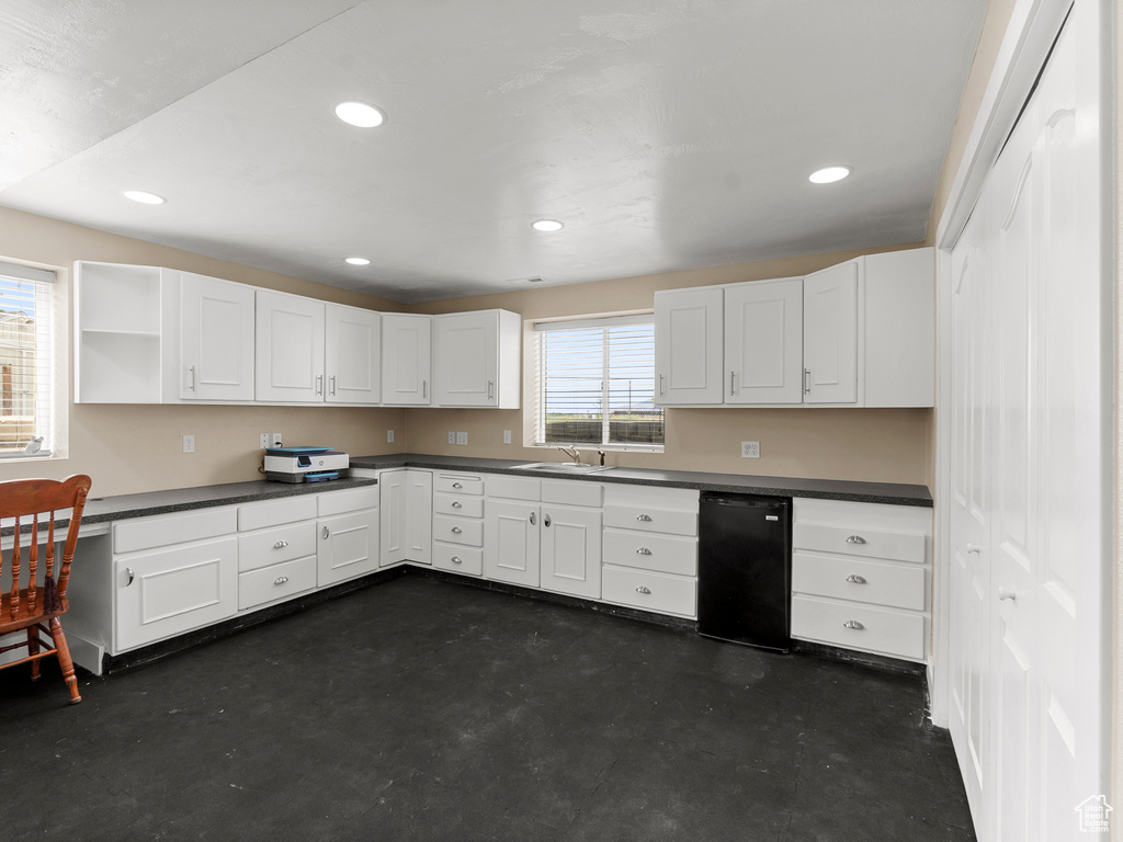 Kitchen featuring a sink, dark countertops, white cabinets, finished concrete flooring, and recessed lighting
