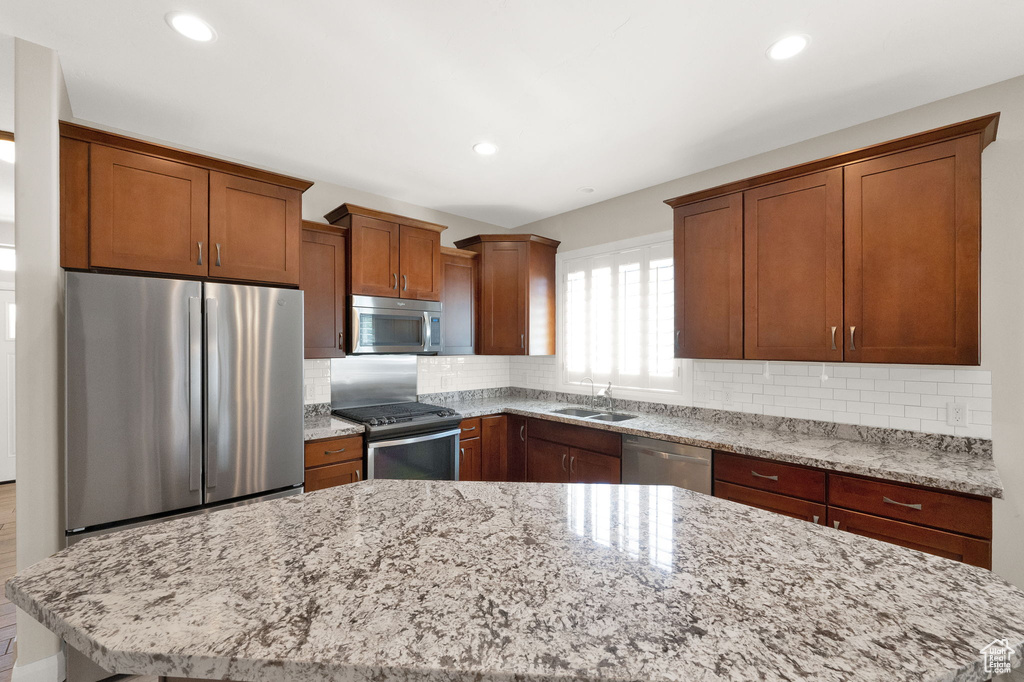 Kitchen with appliances with stainless steel finishes, a sink, light stone countertops, tasteful backsplash, and recessed lighting