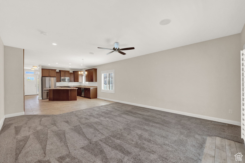 Unfurnished living room with light carpet, a ceiling fan, baseboards, recessed lighting, and a chandelier