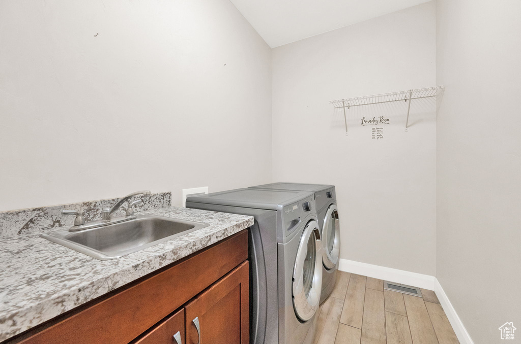 Laundry room with separate washer and dryer, light wood-type flooring, baseboards, and cabinet space