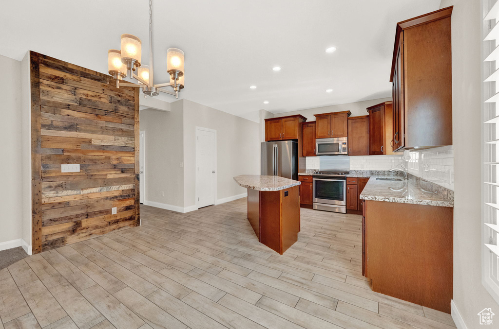 Kitchen with appliances with stainless steel finishes, a center island, light wood-type flooring, a chandelier, and light stone countertops