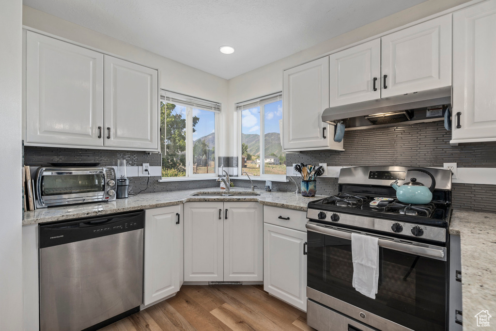 Kitchen with appliances with stainless steel finishes, under cabinet range hood, a sink, backsplash, and white cabinetry