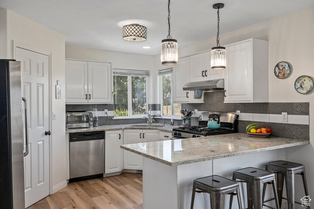 Kitchen featuring stainless steel appliances, under cabinet range hood, a peninsula, a sink, and white cabinets
