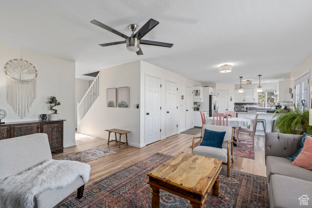 Living room with light wood-style floors, ceiling fan, stairs, and baseboards