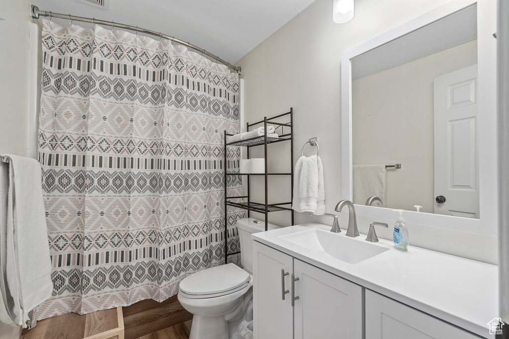 Full bath featuring vanity, toilet, curtained shower, and wood finished floors