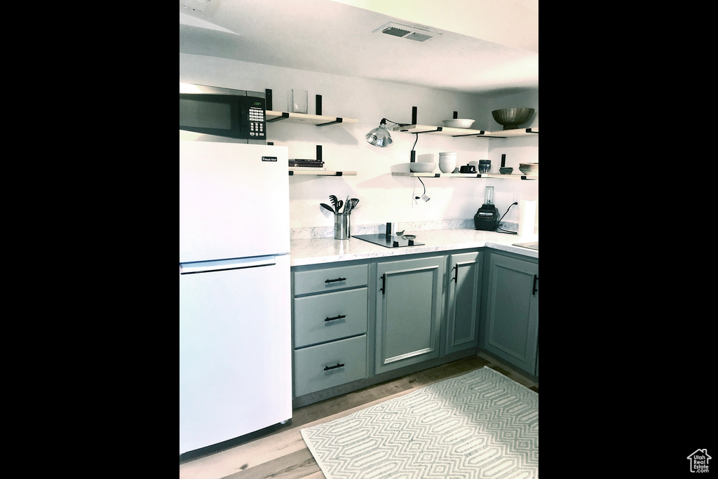 Kitchen with freestanding refrigerator, open shelves, light wood finished floors, and black electric stovetop