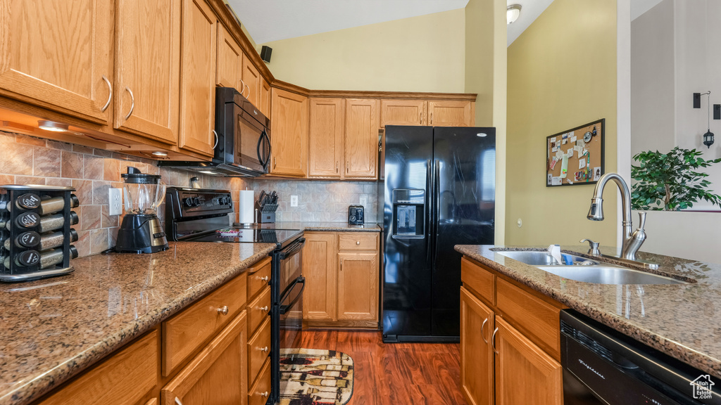 Kitchen featuring black appliances, a sink, vaulted ceiling, dark wood-type flooring, and light stone countertops