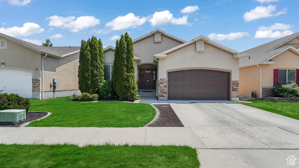 View of front of house featuring stucco siding, an attached garage, driveway, stone siding, and a front lawn