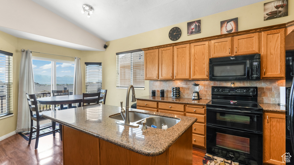 Kitchen with black appliances, a sink, lofted ceiling, decorative backsplash, and a center island with sink