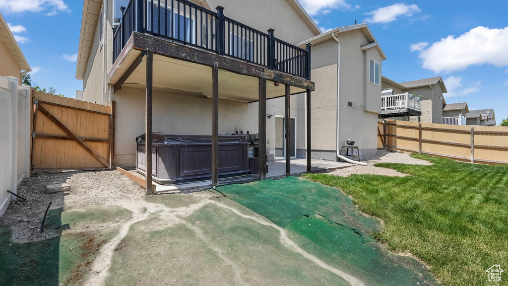 Back of house featuring a hot tub, a patio, stucco siding, a balcony, and a gate