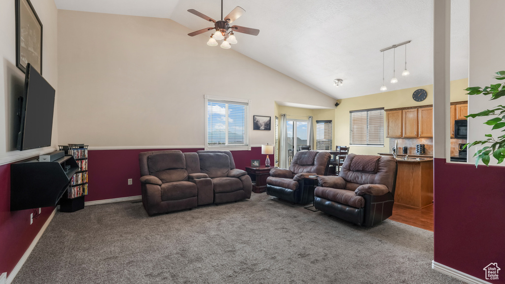 Living room featuring carpet floors, ceiling fan, high vaulted ceiling, and baseboards