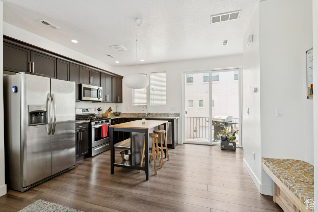 Kitchen with appliances with stainless steel finishes, dark wood-type flooring, dark brown cabinetry, light countertops, and pendant lighting