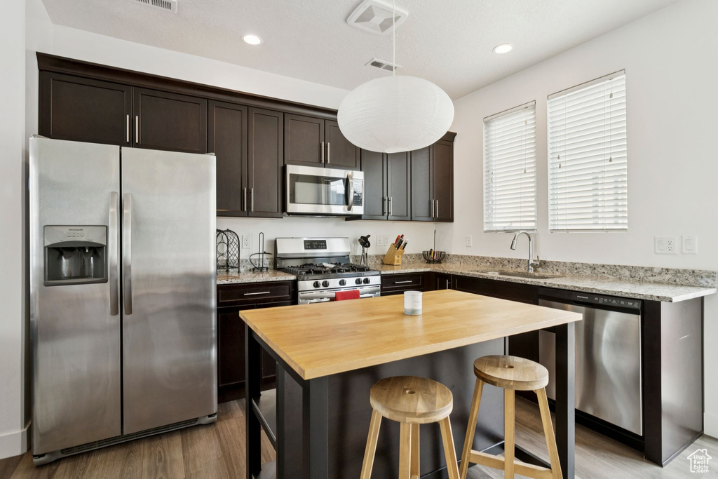 Kitchen featuring appliances with stainless steel finishes, wood counters, a sink, dark brown cabinetry, and light wood-type flooring