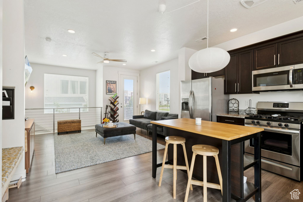Kitchen with appliances with stainless steel finishes, dark brown cabinets, open floor plan, wood counters, and wood finished floors