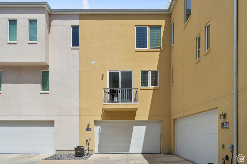Back of house featuring a garage, a balcony, stucco siding, central AC, and driveway