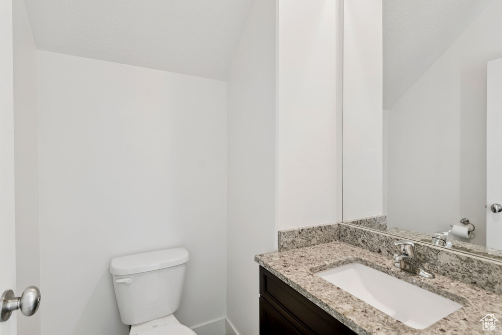 Half bathroom featuring toilet, vanity, vaulted ceiling, and baseboards