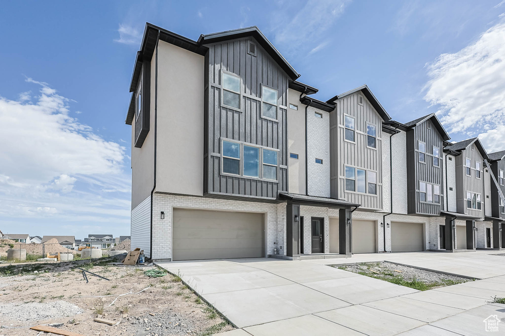 Townhome / multi-family property featuring an attached garage, concrete driveway, a residential view, board and batten siding, and brick siding