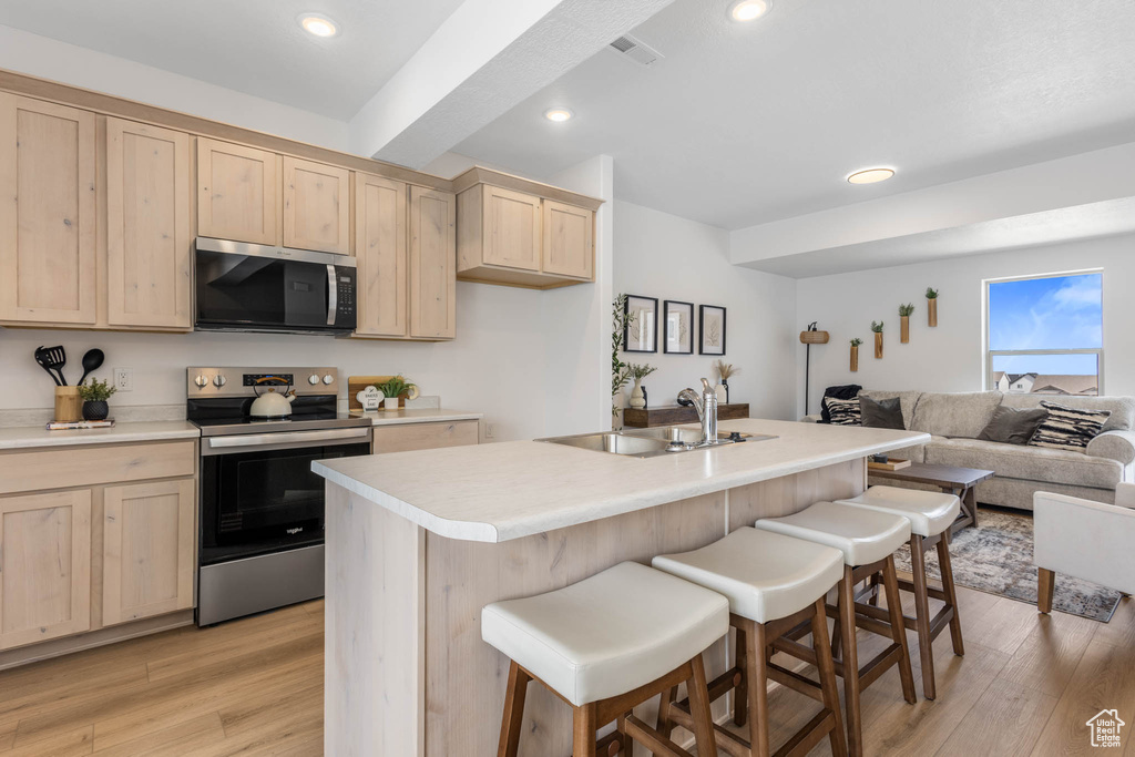 Kitchen with appliances with stainless steel finishes, light brown cabinetry, a sink, open floor plan, and light wood-style flooring