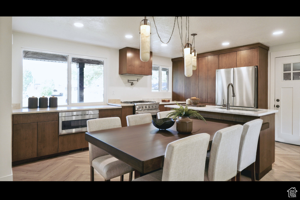 Kitchen with stainless steel appliances, light countertops, hanging light fixtures, a kitchen island with sink, and recessed lighting