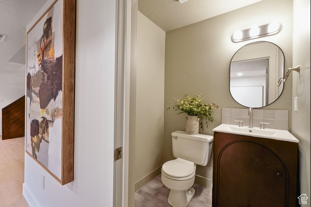 Bathroom with toilet, vanity, wood finished floors, baseboards, and a textured ceiling