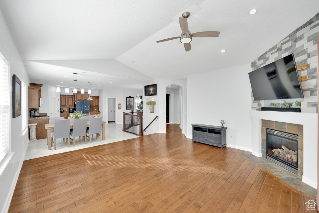 Unfurnished living room featuring a ceiling fan, a tile fireplace, arched walkways, light wood-style flooring, and vaulted ceiling