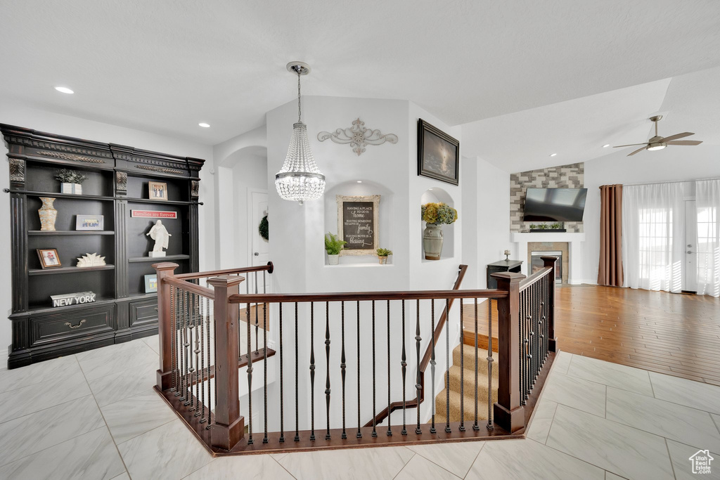 Corridor with an upstairs landing, vaulted ceiling, a chandelier, light marble finish floors, and recessed lighting