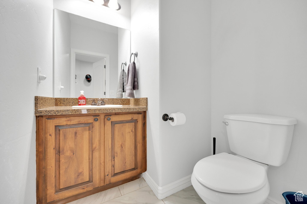 Bathroom featuring marble look tiles, toilet, vanity, and baseboards