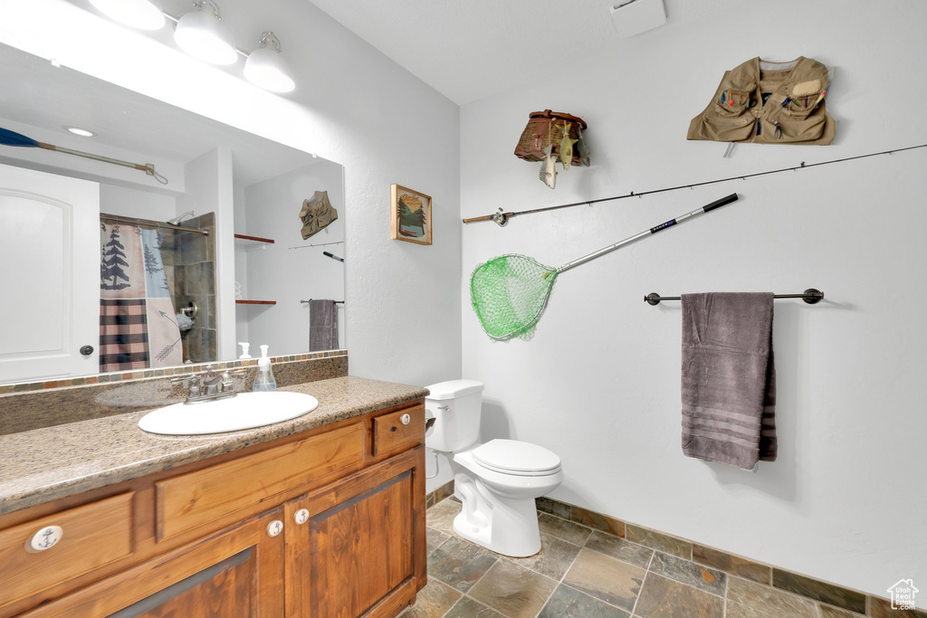 Bathroom featuring stone tile floors, vanity, toilet, baseboards, and a shower with shower curtain