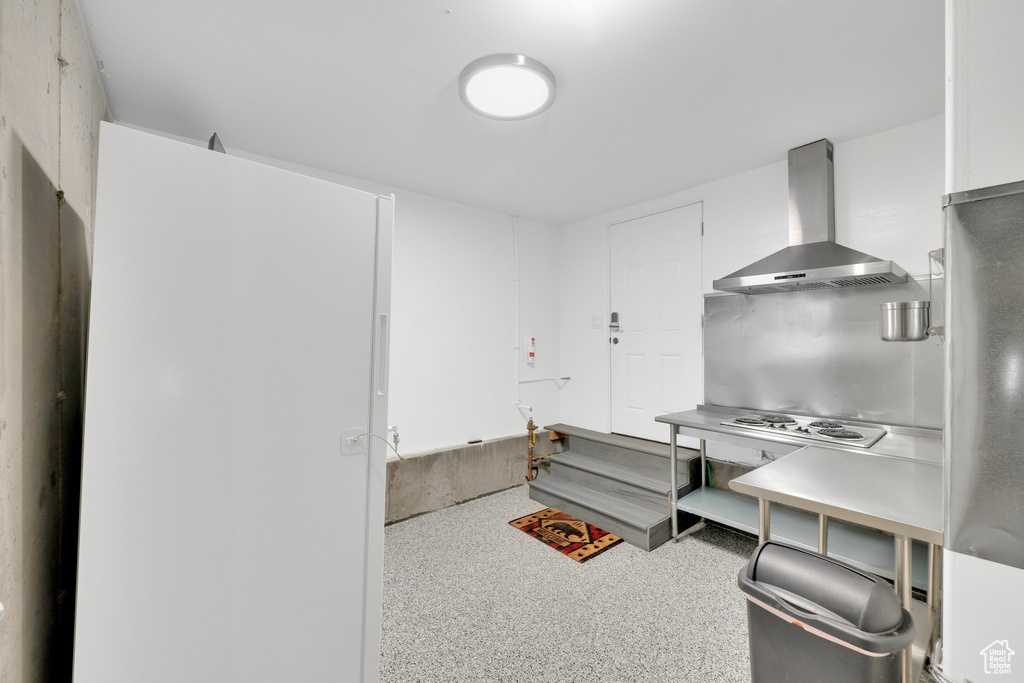 Kitchen with wall chimney exhaust hood, light countertops, and speckle patterned floor