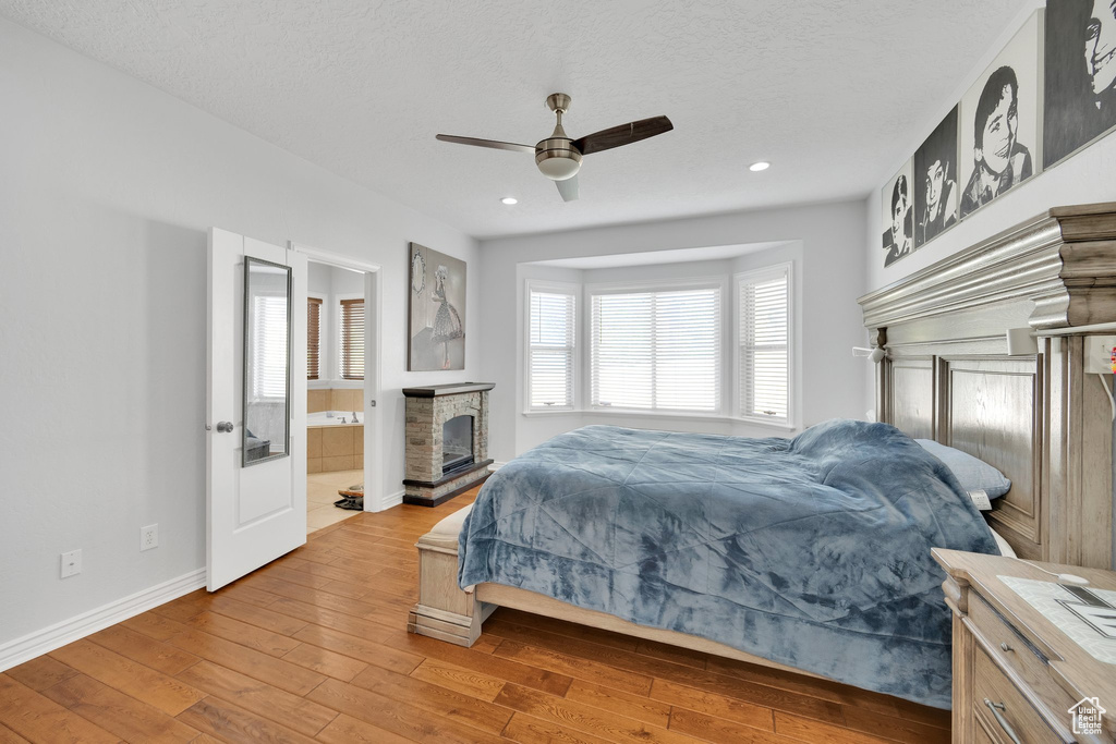 Bedroom with hardwood / wood-style floors, baseboards, a fireplace with raised hearth, recessed lighting, and a ceiling fan